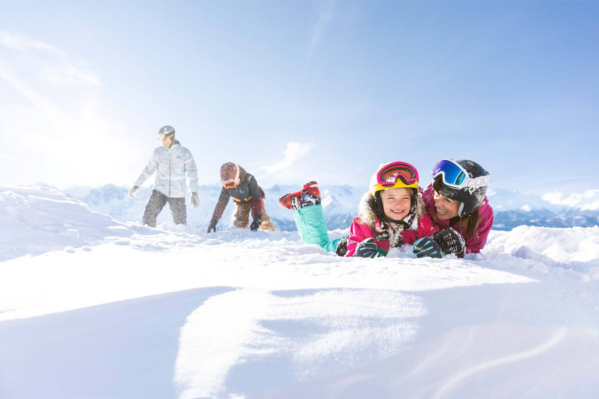 Lachende Familie im Schnee mit Skihelmen und Skibrillen an einem sonnigen Wintertag in Serfaus-Fiss-Ladis