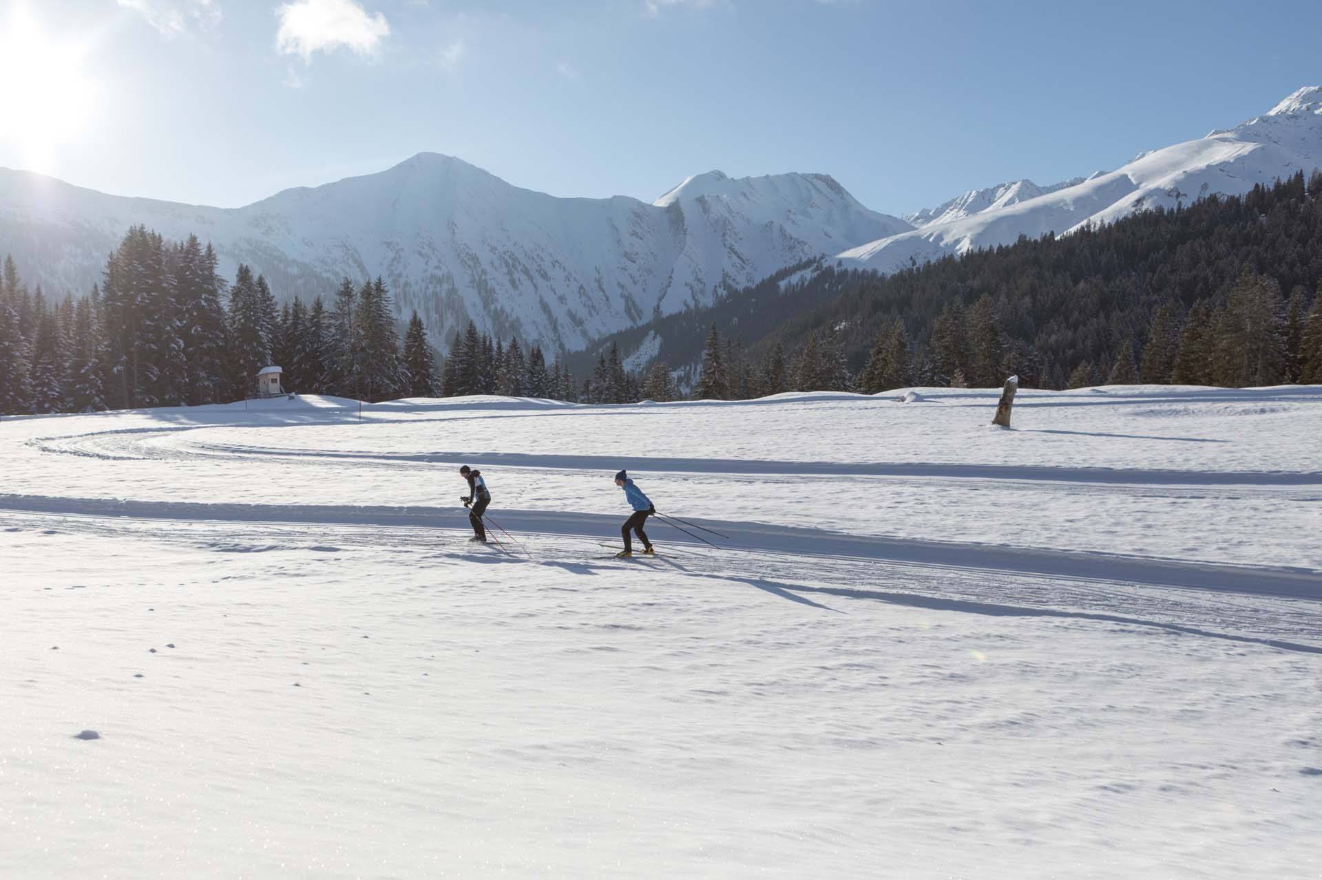 Zwei Langläufer ziehen ihre Spur auf einer präparierten Loipe vor verschneiten Bergen in Serfaus-Fiss-Ladis