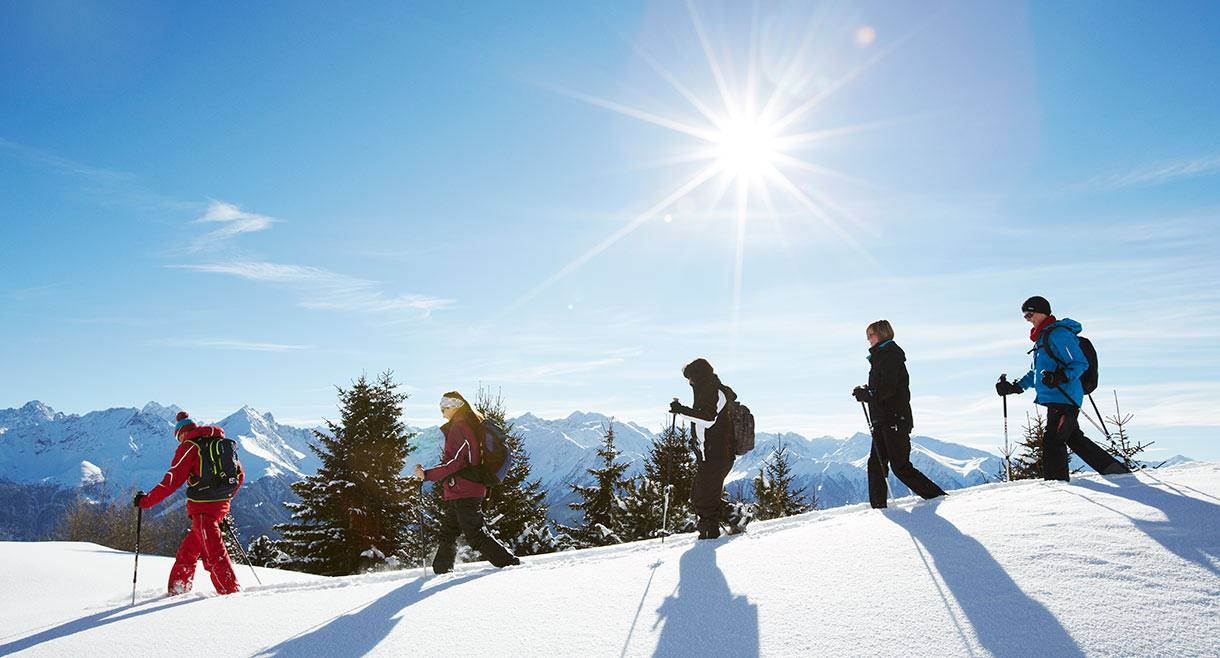 Gruppe beim Schneeschuhwandern in verschneiter Winterlandschaft mit strahlender Sonne in Serfaus-Fiss-Ladis